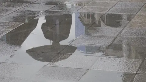 Una persona con paraguas se refleja en un charco provocado por la lluvia esta ma&ntilde;ana en Bilbao.