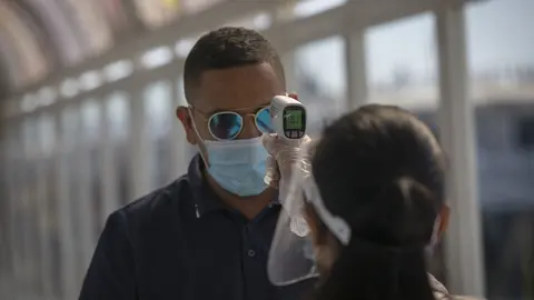 Una trabajadora de la naviera FRS toma la temperatura a un pasajero antes de embarcar durante la reanudaci&oacute;n de la ruta Algeciras-Ceuta, una vez restablecida la circulaci&oacute;n en todo el territorio nacional tras el fin del Estado de Alarma. En el Puerto de A