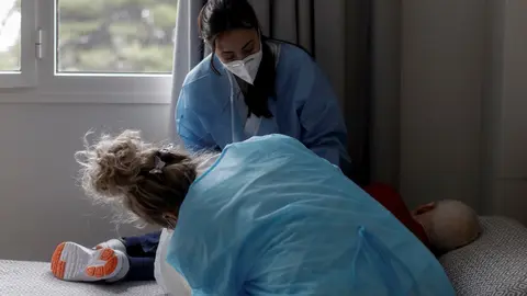 Estefan&iacute;a (de frente), t&eacute;cnico sociosanitario, y Virtu (de espaldas), enfermera, ambas trabajadoras del Centro de Mayores Casablanca Villaverde (Av. de Rafaela Ybarra, 135), asisten a un residente en su cuarto cuatro d&iacute;as despu&eacute;s de que se decretase el fi