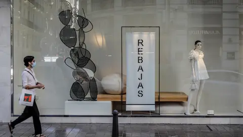 Una mujer protegida con mascarilla pasa al lado del escaparate de una tienda donde se observan carteles indicativos de rebajas en Valencia, Comunidad Valenciana (Espa&ntilde;a) a 3 de julio de 2020. El 61% de los consumidores gastar&aacute; 129 euros de media en las re