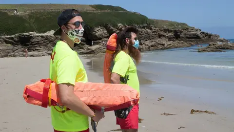 Dos socorristas protegidos con mascarilla vigilan la Playa de A Rapadoira en Foz, en la comarca de A Mari&ntilde;a, Lugo.