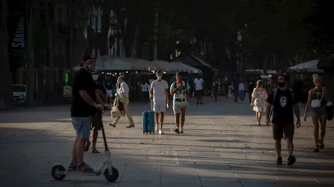 Dos j&oacute;venes caminan, uno de ellos lleva una maleta, en Barcelona, Catalunya (Espa&ntilde;a), a 28 de julio de 2020.