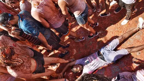 Un joven se tumba en el suelo cubierto con los restos de los tomates arrojados durante la fiesta de la Tomatina de Bu&ntilde;ol 2019.
