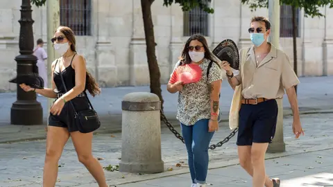 Tres j&oacute;venes pasean con mascarillas y  abanico en el primer d&iacute;a  de uso obligatorio de mascarillas en Sevilla a 15 de julio del 2020