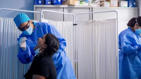 Un trabajador sanitario protegido le realiza a una mujer un test PCR 