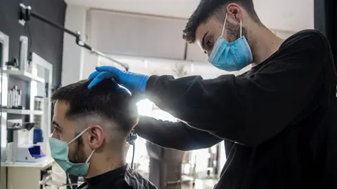 Un peluquero atiende a un cliente en su peluquer&iacute;a 
