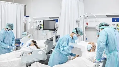 Doctors and nurses taking care of patients in ICU. Team of frontline coworkers are treating man and woman. They are at hospital during COVID-19. (Doctors and nurses taking care of patients in ICU. Team of frontline coworkers are treating man and woman