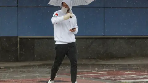 Transe&uacute;ntes protegidos con mascarilla y un paraguas caminan por las calles de la capital un d&iacute;a marcado por la llegada a la pen&iacute;nsula de una borrasca fr&iacute;a que ha activado la alerta por viento o lluvia en 8 comunidades, entre ellas, Madrid, en los inicios 