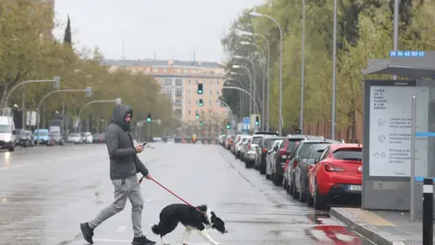 Un joven pasea un perro por el centro de la capital donde las temperaturas han bajado estrepitosamente durante el segundo d&iacute;a de la entrada en vigor de la limitaci&oacute;n total de movimientos salvo de los trabajadores de actividades esenciales, medida adoptada