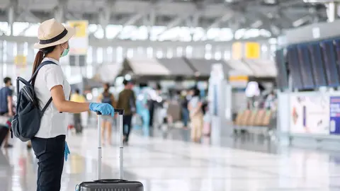 Turistas en aeropuerto con maleta y mascarilla