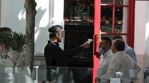 Un camarero mide la temperatura de sus clientes en una c&eacute;ntrica terraza madrile&ntilde;a en el primer d&iacute;a de la Fase 1, cuando se reabren al p&uacute;blico las terrazas al aire libre de los establecimientos de hosteler&iacute;a y restauraci&oacute;n limit&aacute;ndose al 50% de las mesas y