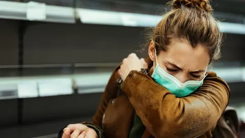 Sick woman buying in supermarket and coughing into elbow during COVID-19 pandemic. 