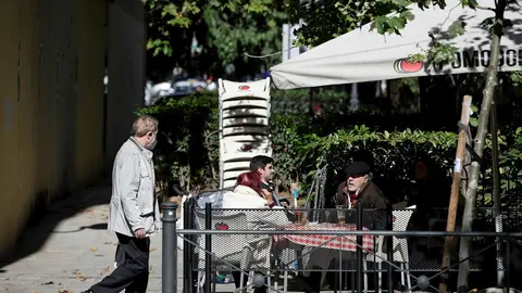 Un hombre camina frente a la terraza de un bar donde hay sentadas otras tres personas en la zona b&aacute;sica de salud de Guzm&aacute;n el Bueno, en el distrito de Chamber&iacute;, en Madrid (Espa&ntilde;a), a 26 de octubre de 2020. Guzm&aacute;n el Bueno es una de las zonas b&aacute;sicas de sa