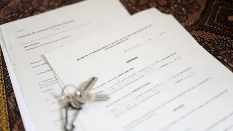 Unas llaves sobre un contrato de compraventa de vivienda y un contrato de arrendamiento (alquiler) de una habitaci&oacute;n en una vivienda compartida.