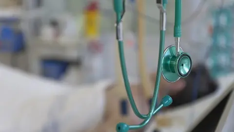 Green stethoscope, on background patient  connected to medical ventilator in ICU in hospital, a place where can be treated patients with pneumonia caused by coronavirus covid-19. (Green stethoscope, on background patient  connected to medical ventilat