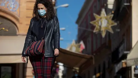 Una mujer con mascarilla camina por la plaza de San Francisco, al fondo las luces del alumbrado de navidad de la calle Sierpes, en Sevilla (Andaluc&iacute;a, Espa&ntilde;a), a 20 de noviembre de 2020.