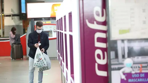 Un viajero con mascarilla obtiene un billete en un dispensador en la estaci&oacute;n de Atocha