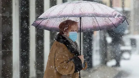 Una mujer se cubre de la nieve con un paraguas en Becerrea, en Lugo, Galicia (Espa&ntilde;a), a 4 de diciembre de 2020. Hoy se ha producido la primera gran nevada del oto&ntilde;o en la monta&ntilde;a lucense. La intensa nevada que est&aacute; cayendo sobre el centro de la provincia