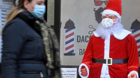 Una mujer con mascarilla pasando junto a un Pap&aacute; Noel con mascarilla en Palermo, Sicilia, Italia