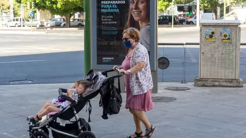 Una se&ntilde;ora con mascarillas pasea a dos ni&ntilde;os ante un cartel publicitario en el primer d&iacute;a  de uso obligatorio de mascarillas en Sevilla a 15 de julio del 2020