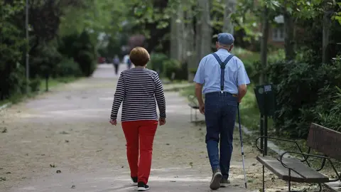 Una mujer y un hombre de edad avanzada con bast&oacute;n caminan por Madrid.
