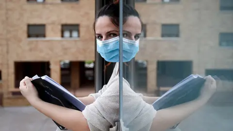 Una mujer con una mascarilla lee asomada a la ventana de su casa cuando queda tan solo una semana para que ni&ntilde;os y preadolescentes puedan salir a la calle durante el confinamiento por el coronavirus, en Valdemoro/Madrid (Espa&ntilde;a) a 20 de abril de 2020.