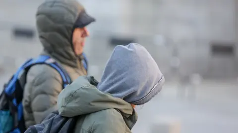 Dos jovenes se protegen del fr&iacute;o con abrigos y gorros mientras pasean durante un d&iacute;a de fr&iacute;o y viento por Madrid
