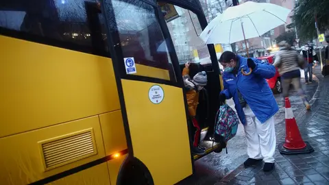Una trabajadora ayuda a bajar a un alumno de un autob&uacute;s escolar del colegio Arcangel Rafael el d&iacute;a de la reapertura de los centros educativos tras la gran nevada registrada por el paso de &lsquo;Filomena&rsquo;, en Aluche, Madrid, (Espa&ntilde;a), a 20 de enero de 2021. El 