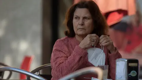 Una mujer en la terraza de un bar con la mascarilla en la mano, mientras contin&uacute;a el cierre perimetral en Montequinto, Dos Hermanas, (Sevilla, Andaluc&iacute;a, Espa&ntilde;a), a 28 de enero de 2020.
