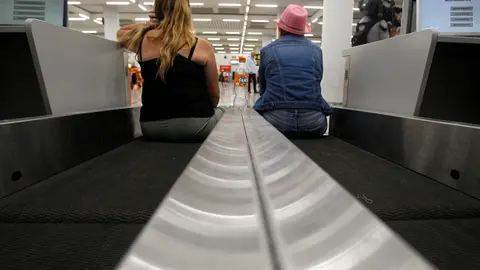 Dos turistas esperan sentadas en una cinta transportadora de maletas en el aeropuerto de Palma de Mallorca (Baleares), horas despu&eacute;s de que la compa&ntilde;&iacute;a brit&aacute;nica Thomas Cook anunciase su quiebra y de que varios de sus vuelos fuesen cancelados, a 23 de sep