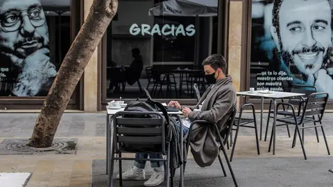 Un joven trabaja con su ordenador port&aacute;til en una terraza el primer d&iacute;a de la apertura de la hosteler&iacute;a en Valencia, Comunidad Valenciana (Espa&ntilde;a), a 1 de marzo de 2021. Coincidiendo con el inicio de la desescalada en la regi&oacute;n, la hosteler&iacute;a de la Comuni