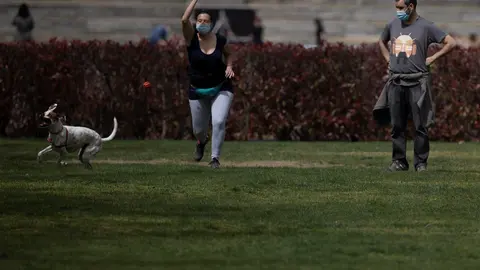 Archivo - Un hombre y una mujer, con mascarilla, juegan con un perro en el Parque del Manzanares, el d&iacute;a en que entra en vigor el uso obligatorio de mascarilla incluso con distancia de seguridad, en Madrid (Espa&ntilde;a), a 31 de marzo de 2021. Hoy entra en vig