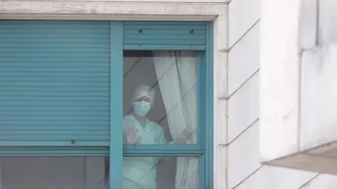 Archivo - Una trabajadora del personal sanitario protegida con mascarilla se asoma por una de las ventanas de una residencia de Madrid.