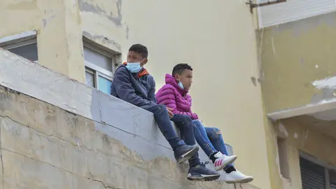 Dos ni&ntilde;os sentados sobre un muro en la nave de primera acogida del pol&iacute;gono del Tarajal en Ceuta (Espa&ntilde;a)