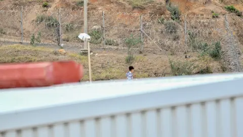Un ni&ntilde;o camina por un tejado al tratar de escapar de la nave de primera acogida del pol&iacute;gono del Tarajal, en Ceuta (Espa&ntilde;a).