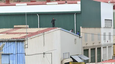 Varios ni&ntilde;os caminan por un tejado al tratar de escapar de la nave de primera acogida del pol&iacute;gono del Tarajal, en Ceuta.