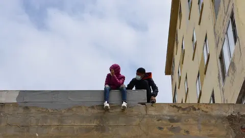 Dos ni&ntilde;os sentados sobre un muro en la nave de primera acogida del pol&iacute;gono del Tarajal.