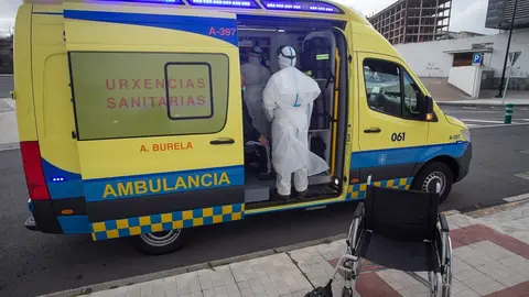 Archivo - Un trabajador sanitario totalmente protegido ayuda a subir a la ambulancia a un anciano de una residencia en Galicia.