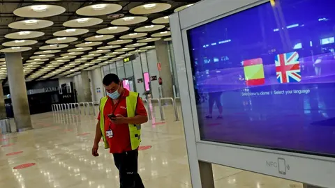 Archivo - Un operario de Iberia pasa al lado de un monitor con las banderas de Espa&ntilde;a y Reino Unido en la T1 del Aeropuerto de Madrid-Barajas Adolfo Su&aacute;rez, en Madrid (Espa&ntilde;a), a 27 de julio de 2020. 