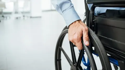 Businessman in wheelchair, hand on wheel close up, office interior on background