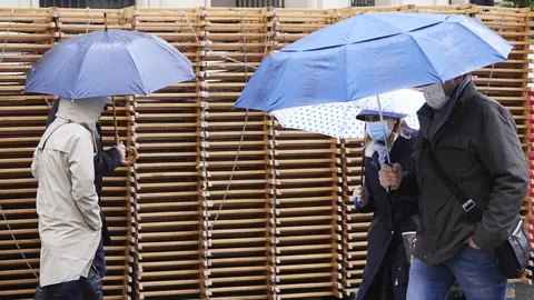 Varias personas pasean con sus parag&uuml;as con las sillas apiladas de fondo durante la vuelta de la lluvia a Sevilla en plenos montaje de los palcos para la Semana Santa, a 5 de abril de 2022 en Sevilla (Andaluc&iacute;a, Espa&ntilde;a)

