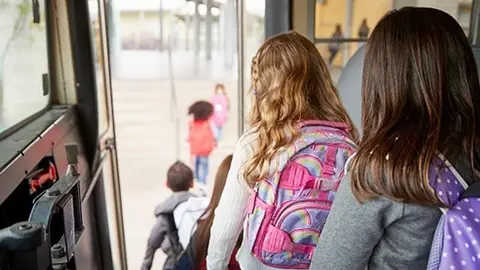 Two girls waiting behind their friends to get off school bus