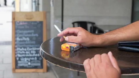 Lugo. Entra en vigor este jueves 13 de agosto una normativa de la Xunta de Galicia por la cual se prohibe fumar en la calle, incluidas las terrazas de los bares, para prevenir los contagios por la Covid19. En la imagen, un hombre sujeta un cigarrillo junto al paquete de tabaco en una terraza de la Ronda da Muralla en la manana del jueves 13 de agosto