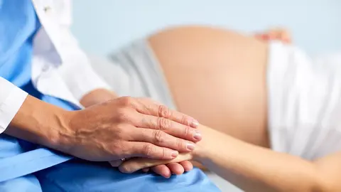 Hand of assistant or nurse holding that of pregnant female