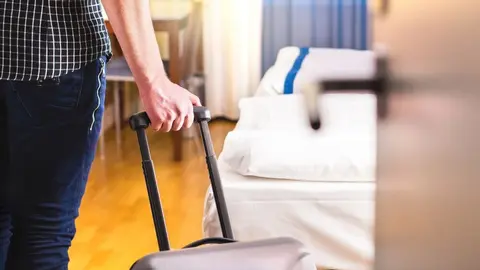 Man pulling suitcase and entering hotel room. Traveler going in to room or walking inside motel with luggage. Travel and holiday apartment rental concept.