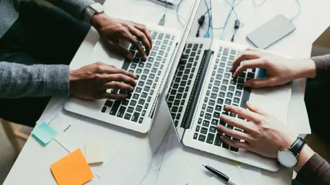 View of an african american and caucasian man collaborating on two laptops