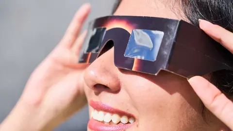 Smiling young latin woman watching an eclipse of the sun with eclipse glasses