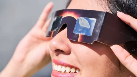 Smiling young latin woman watching an eclipse of the sun with eclipse glasses